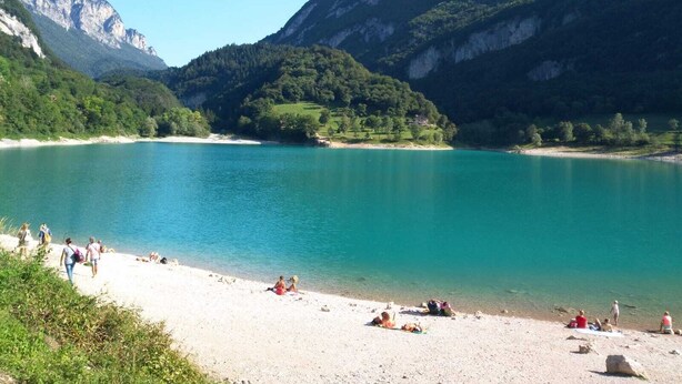 Een strand met helder turquoise water, omringd door weelderige groene heuvels en bergen.