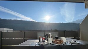 Een tafel buiten, met uitzicht op een berg, een waterkoker, mokken en een stukje taart.