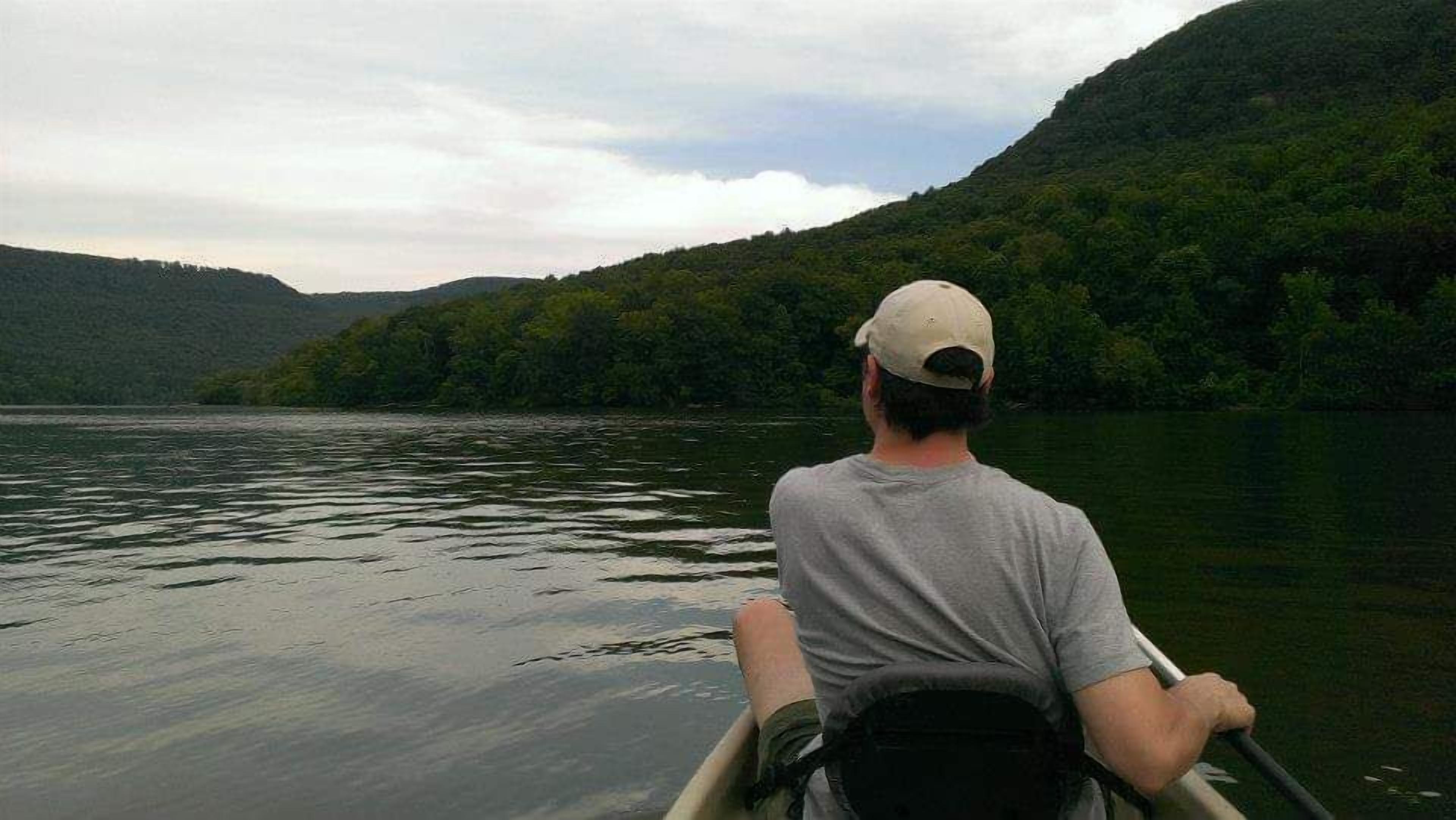 A person in a canoe on a calm lake with hills in the background.