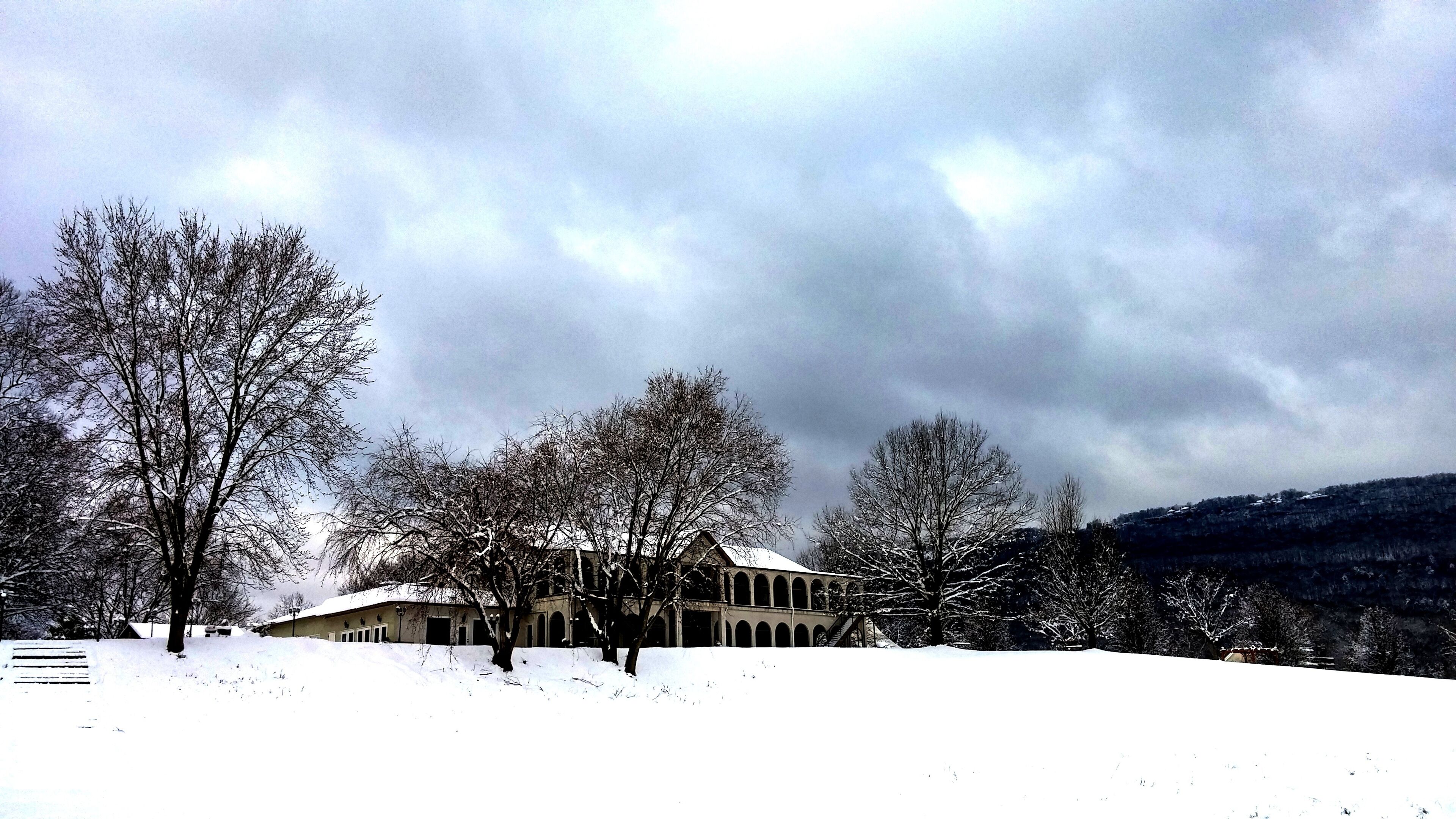 A building with a snow-covered roof and arched windows, surrounded by bare trees and a snowy landscape.