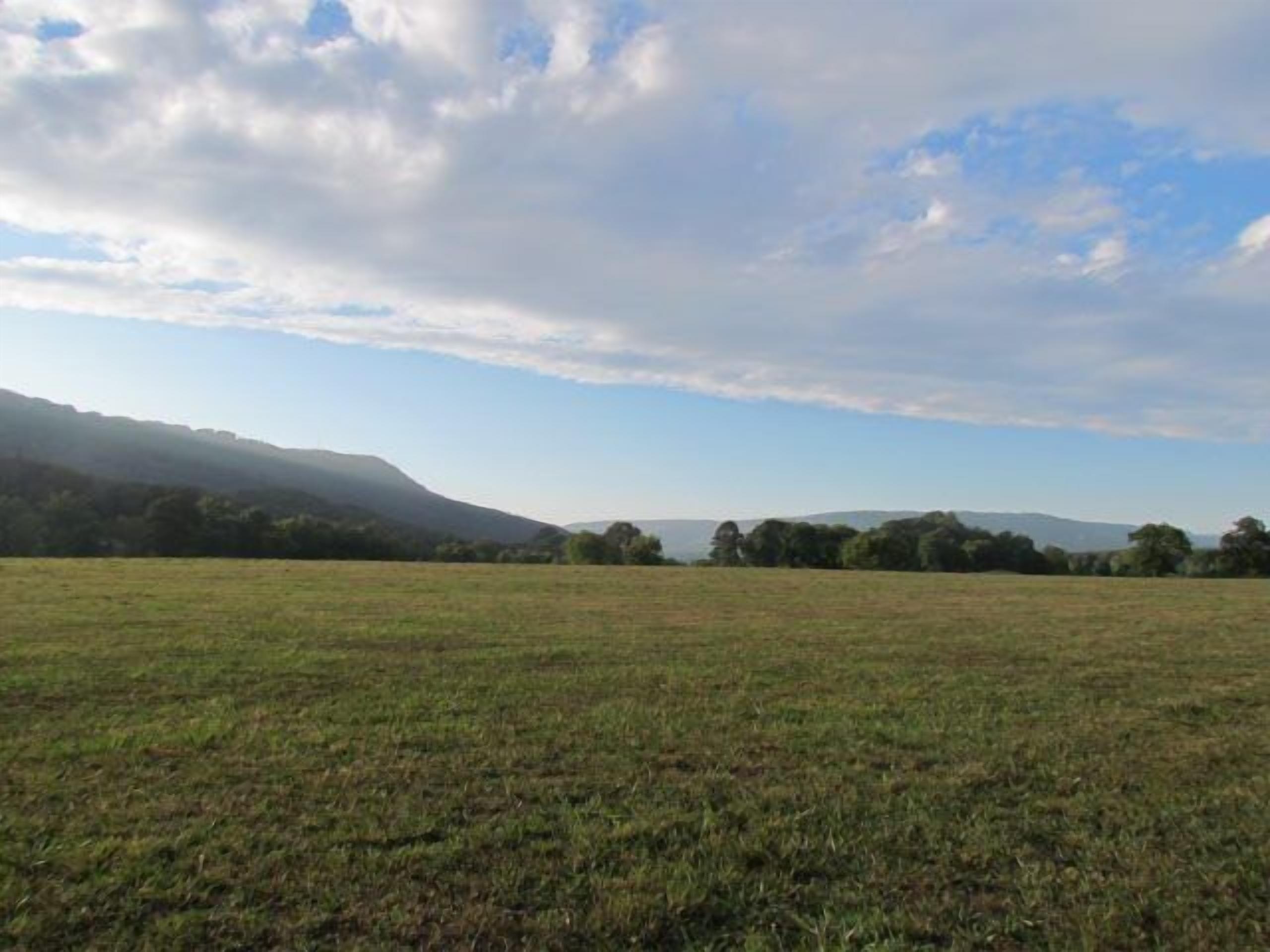 A vast open field with distant hills and a partly cloudy sky.