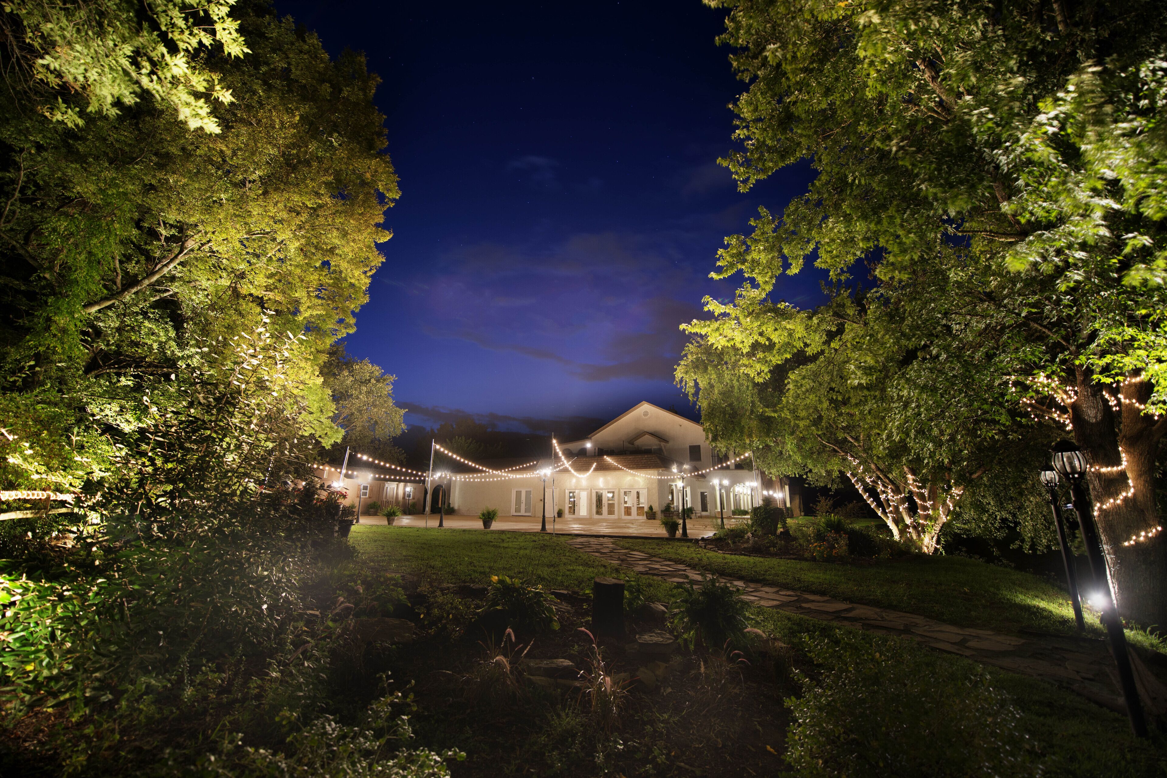 Une maison avec un chemin menant à l’entrée, entourée d’arbres et illuminée de guirlandes lumineuses.
