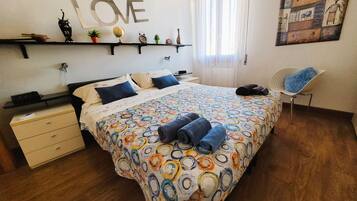 Ein Schlafzimmer mit einem Bett, einem Sessel, einem Regal mit Dekoration und einem Wandbild mit der Aufschrift 'LOVE', sowie einem Gemälde.