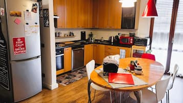 Una cocina compacta con armarios de madera, un refrigerador de acero inoxidable y una mesa de comedor con sillas.