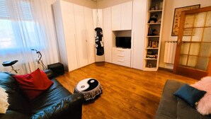 A living room with a black leather sofa, a grey sofa, a wooden floor, a TV, a bookshelf, and a bicycle. - FLORENCE HOMEAWAY - COZY APARTMENT NEAR FLORENCE AIRPORT -18 min from City center (Firenze)