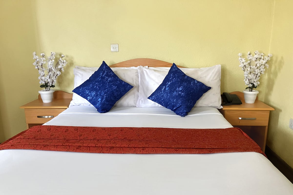A bed with a white and red bedspread, two blue pillows, and white flowers in pots on either side.