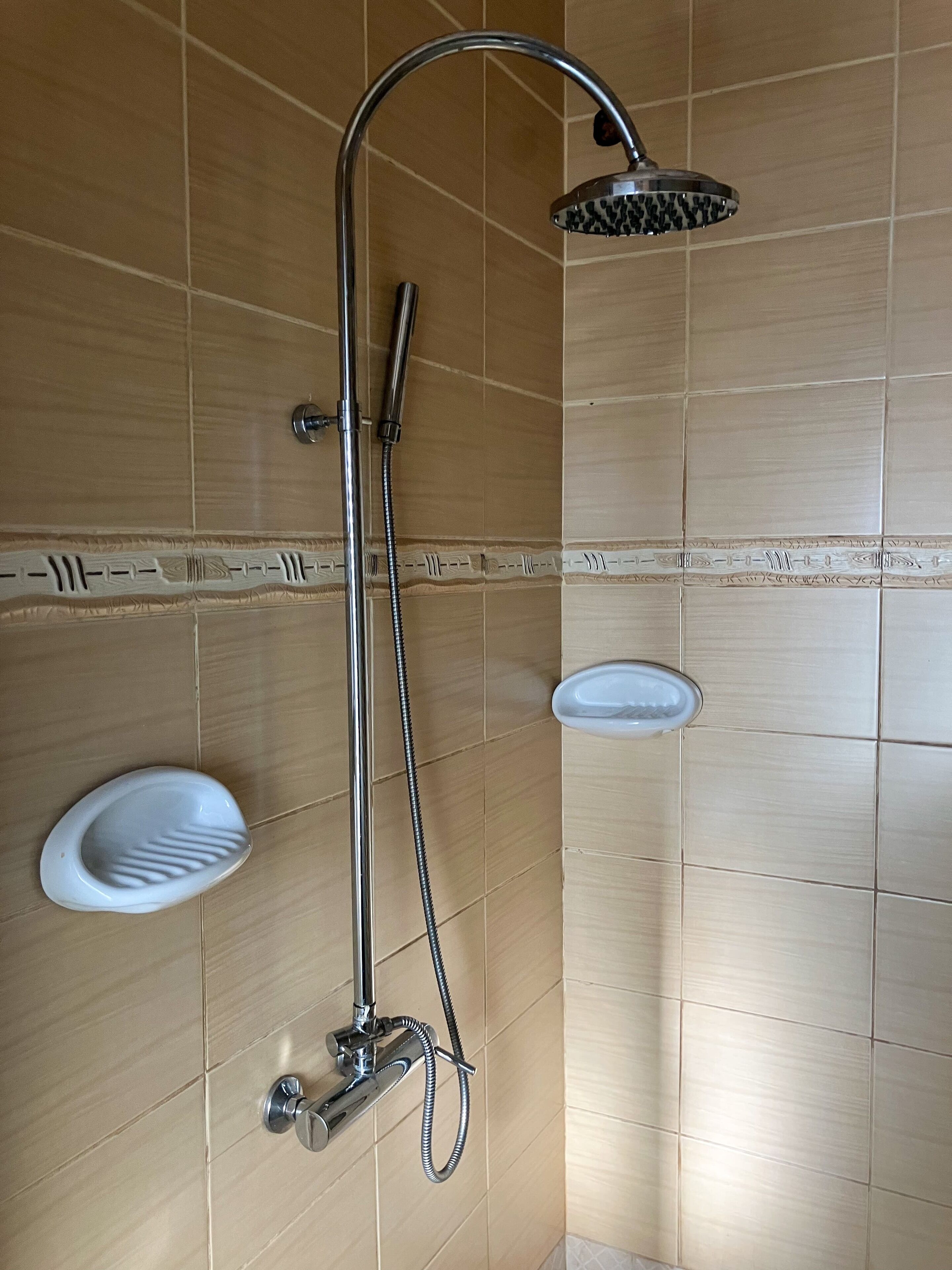 En dusch med ett duschmunstycke som kan hållas i handen och en väggmonterad blandare.