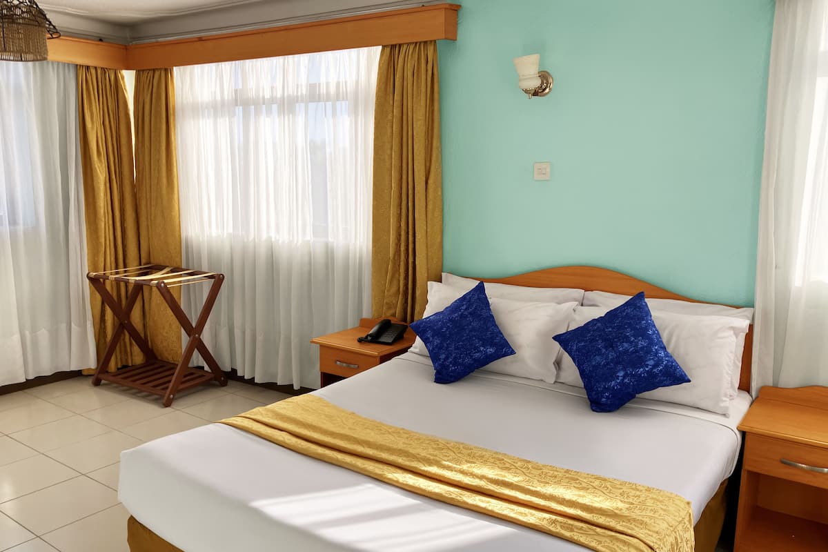 A hotel room with a bed, a wooden nightstand, a telephone, and a wall-mounted light fixture.