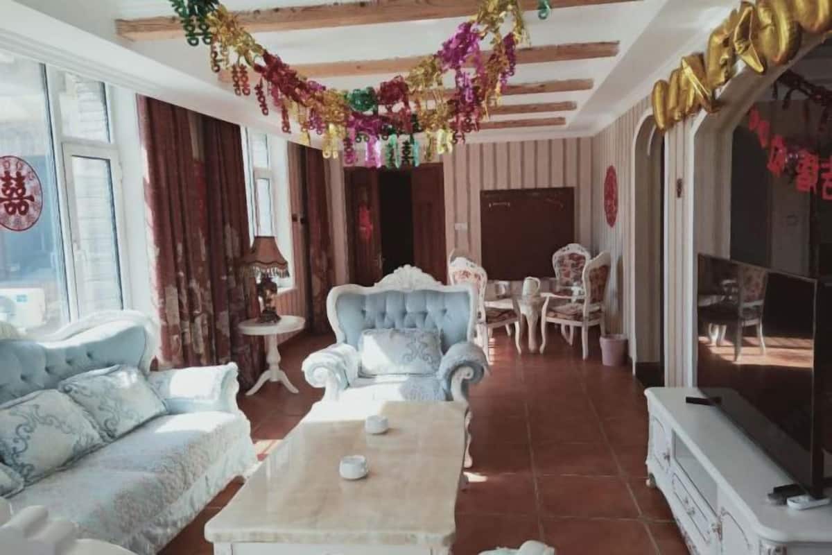 A traditional room with a sofa, armchair, and a small table. There is a television on the right side.