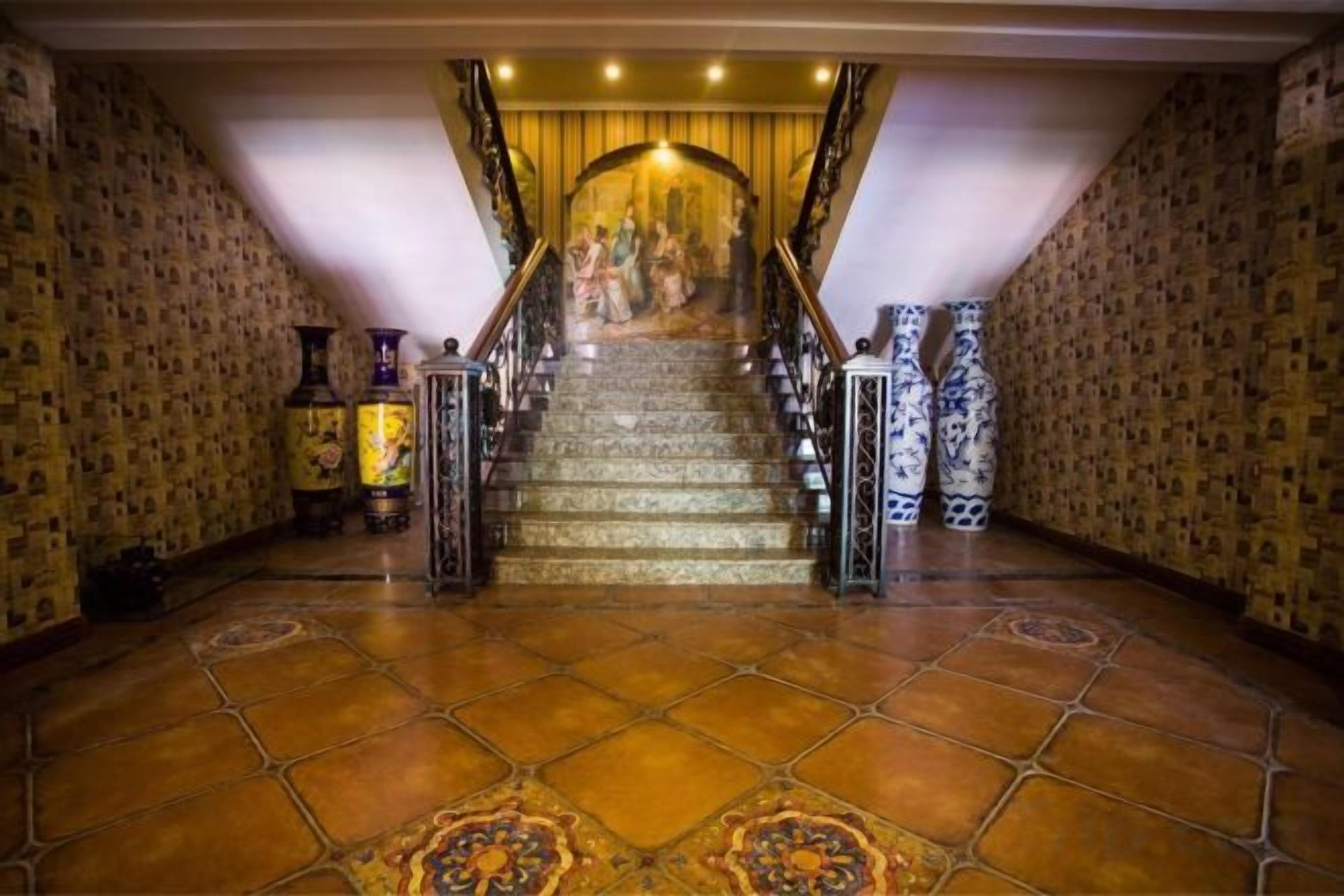 Un magnifique escalier orné de balustrades travaillées, menant à une pièce aux murs décorés de motifs et au sol carrelé.
