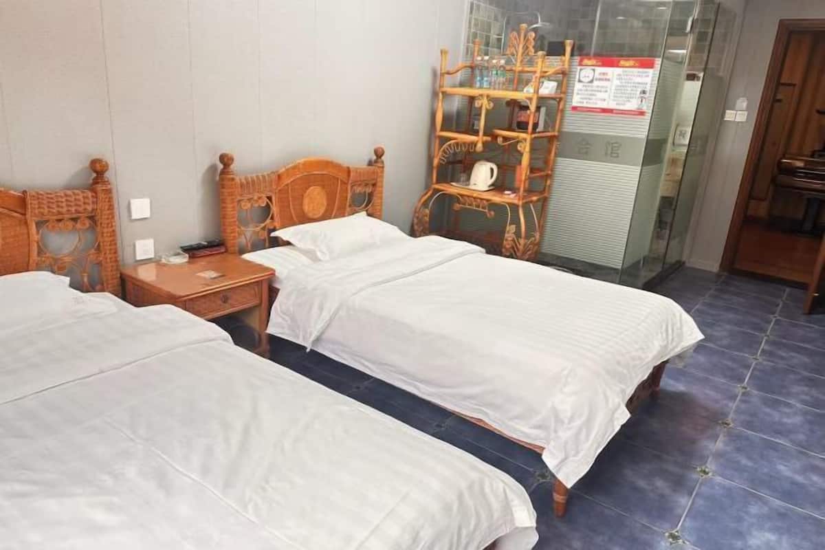 A hotel room with two single beds, a wooden nightstand, a glass partition, and a wooden shelf with a kettle.