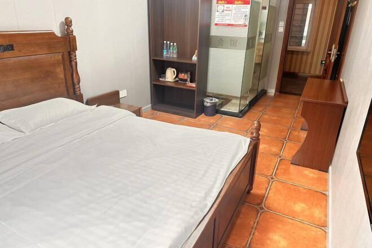A hotel room with a wooden bed, a small shelf with toiletries, and a tiled floor.