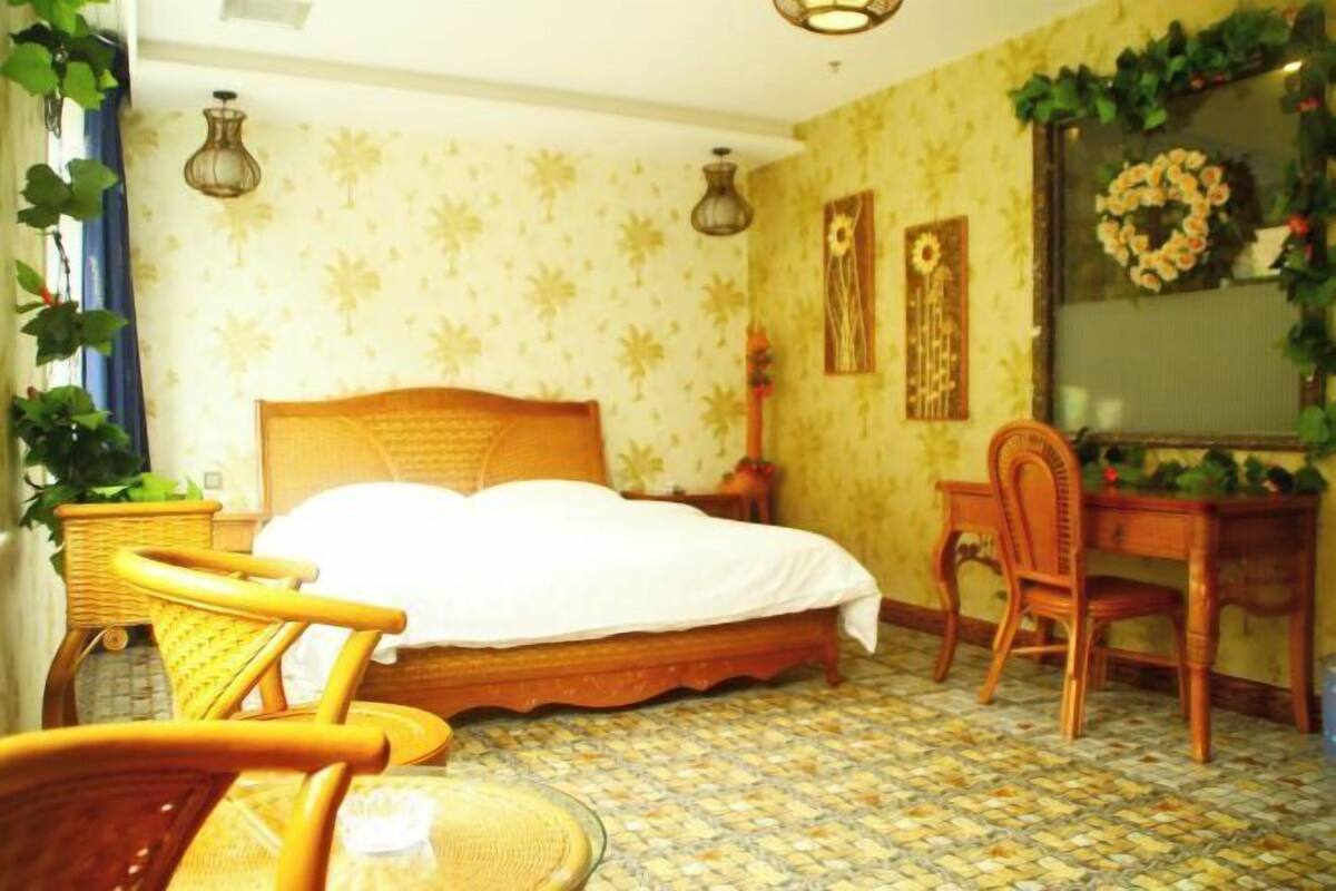 A room with a bed, wicker chairs, a desk, and a patterned floor.