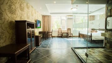 Habitación de hotel con un ventanal grande, una cama, un escritorio, una silla, un televisor y un armario.