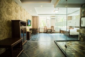 Une chambre d’hôtel avec une grande fenêtre, un lit, un bureau, une chaise, une télévision et une armoire.