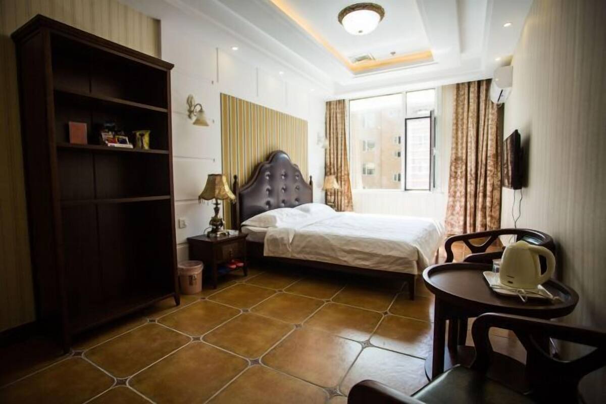 A hotel room with a bed, bedside table, lamp, wardrobe, and a small dining table with chairs.