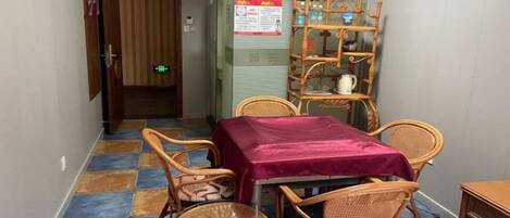 A room with a table and chairs, a wooden shelf unit, and a door leading to another area.