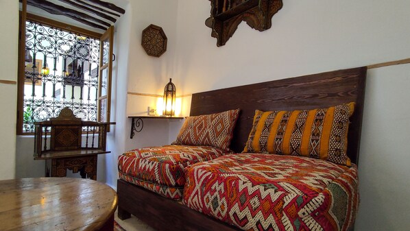 A bedroom with a wooden bed, patterned bedding, a wooden table, and a window with decorative iron bars. - Dar En-Nawat (Marrakech)