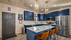 Een moderne keuken met blauwe kastjes, roestvrijstalen apparatuur en een centraal eiland met barkrukken.