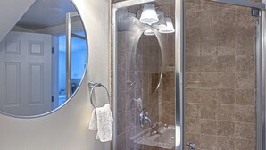 A modern bathroom with a glass-enclosed shower, a round mirror, and a towel rack. - 79-4 spacious studio Walk to backus hospital and downtown (Norwich)