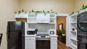 Una cucina compatta con mobili bianchi, un frigorifero nero, un forno a microonde, un fornello e un lavello.