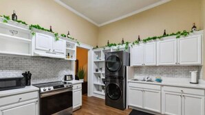 Una cucina moderna con mobili bianchi, un forno in acciaio inossidabile, lavatrice e asciugatrice integrate e piante verdi sugli scaffali.
