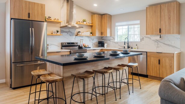 Una cocina moderna con refrigerador de acero inoxidable, armarios de madera, encimera de mármol y taburetes de bar.
