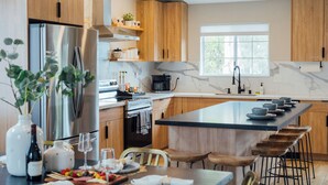 Una cocina moderna con armarios de madera, un refrigerador de acero inoxidable, encimera de mármol y una isla grande con taburetes de bar.