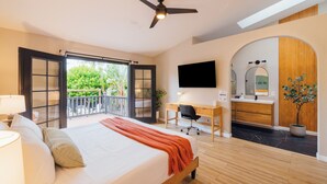 Una habitación de hotel moderna con una cama grande, un escritorio, una silla, un televisor y un balcón con vistas a zonas verdes.