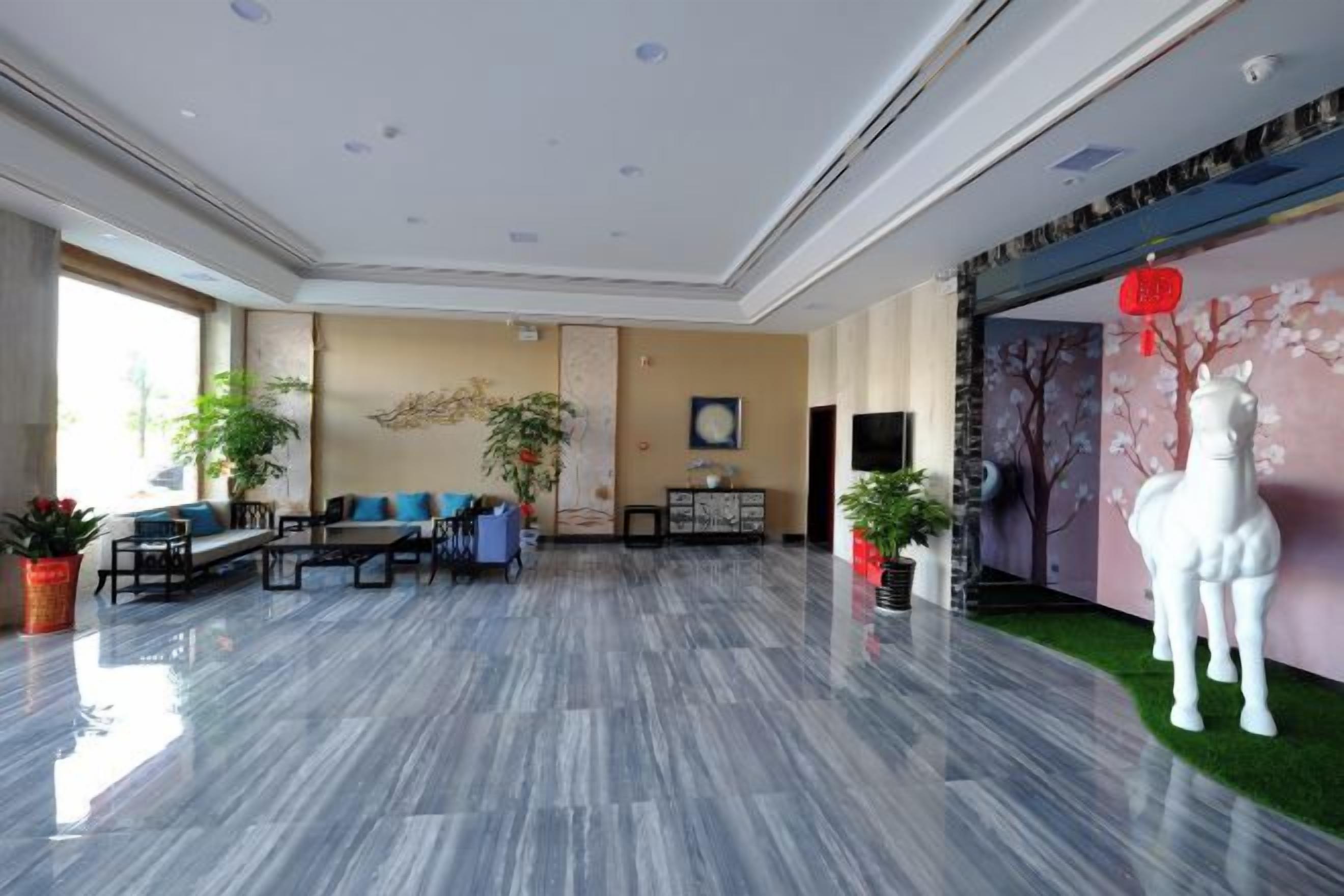 A spacious lobby with a marble floor, seating area, and decorative elements like plants and a horse statue.