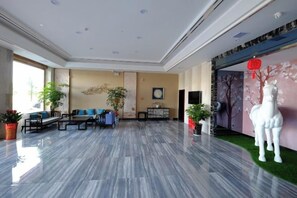 A spacious lobby with a marble floor, seating area, and decorative elements like plants and a horse statue. - Junhao Hotel (Linwu)