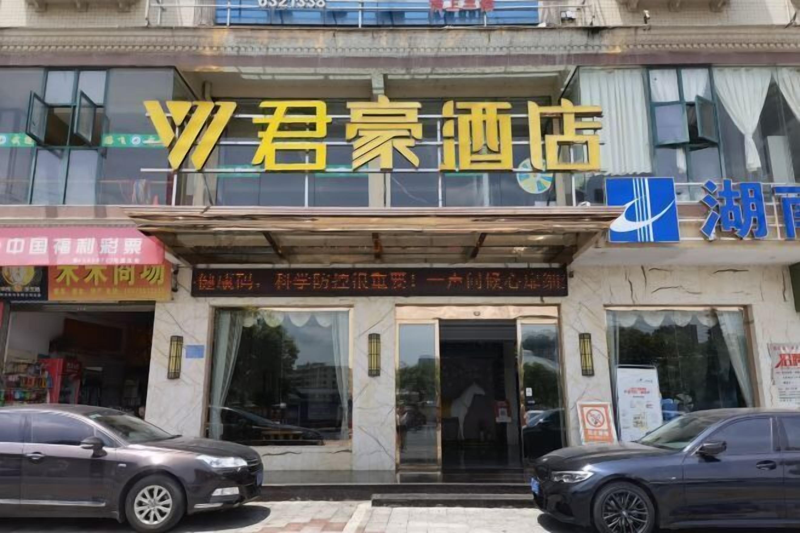 A hotel entrance with a large sign above the door, a car parked in front, and a building facade with various signs and windows.