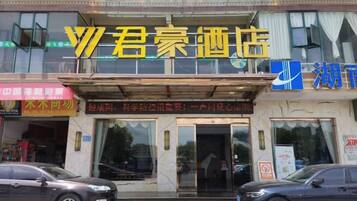 A hotel entrance with a large sign above the door, a car parked in front, and a building facade with various signs and windows.