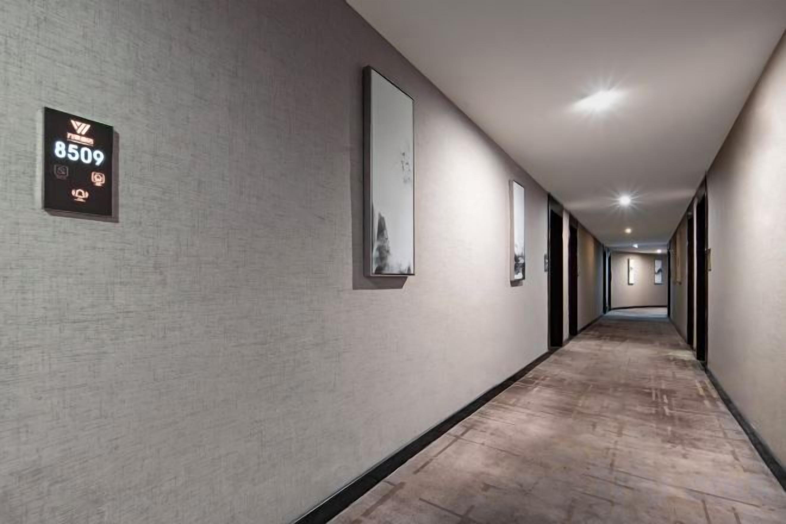 A long, narrow hotel corridor with a textured wall, a sign with the number 8509, and framed pictures on the walls.