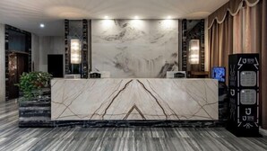 A reception area with a marble counter, wall-mounted lamps, and a large screen. - Junhao Hotel (Linwu)