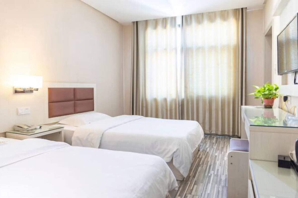 A hotel room with two beds, a desk with a lamp, a TV, and a plant.