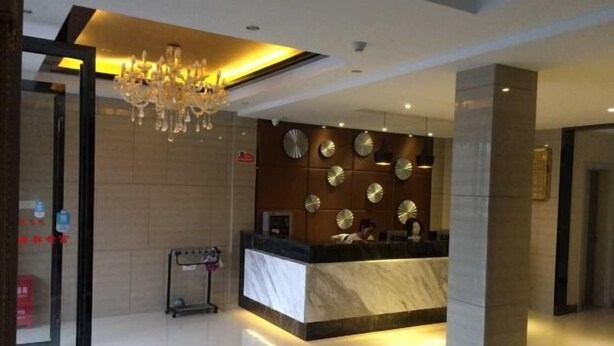 Zona de recepción de un hotel con mostrador de mármol, una araña y relojes en la pared.