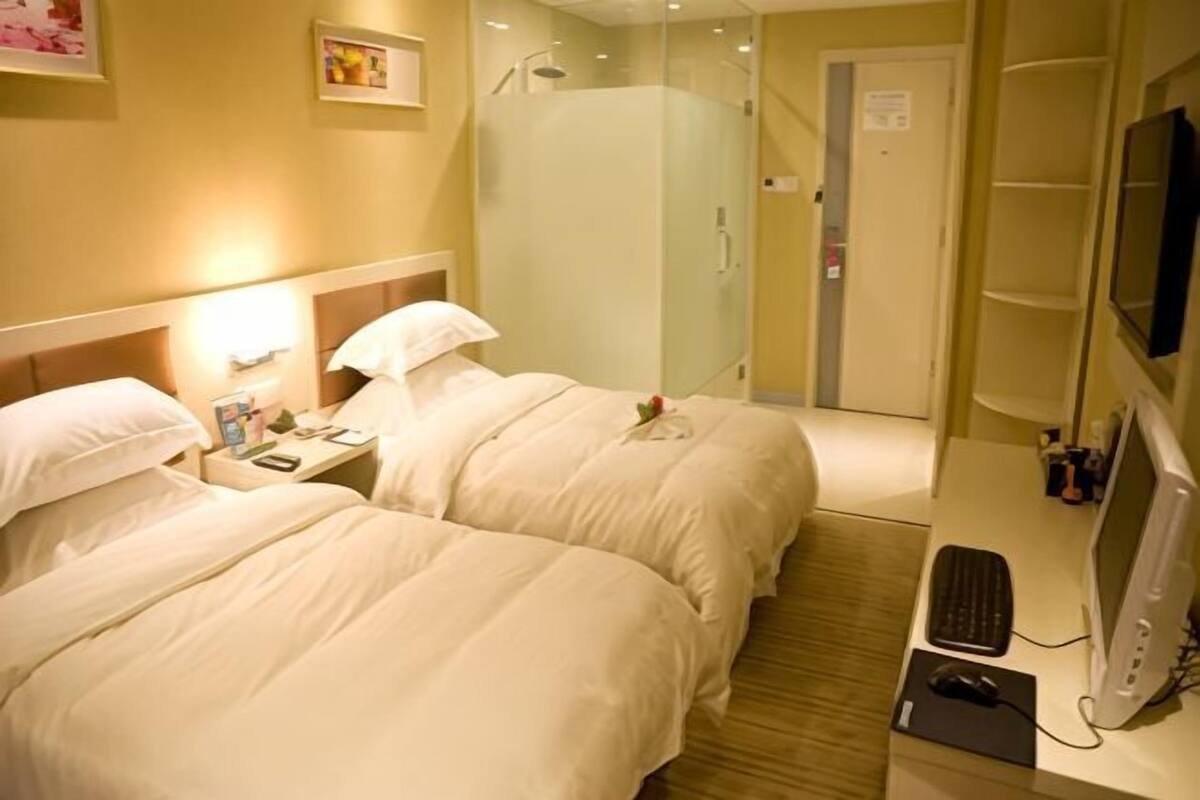 A hotel room with two beds, a desk with a computer, a shower, and a TV.