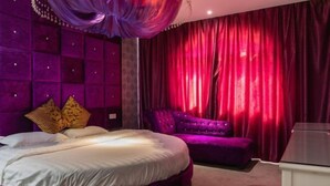Un dormitorio con una cama grande, un sofá púrpura y una mesita.