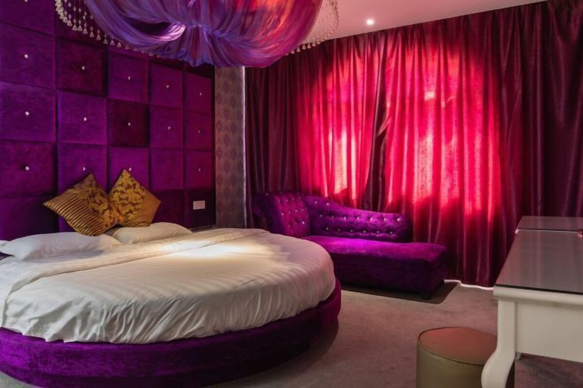 A bedroom with a large bed, a purple sofa, and a small table.