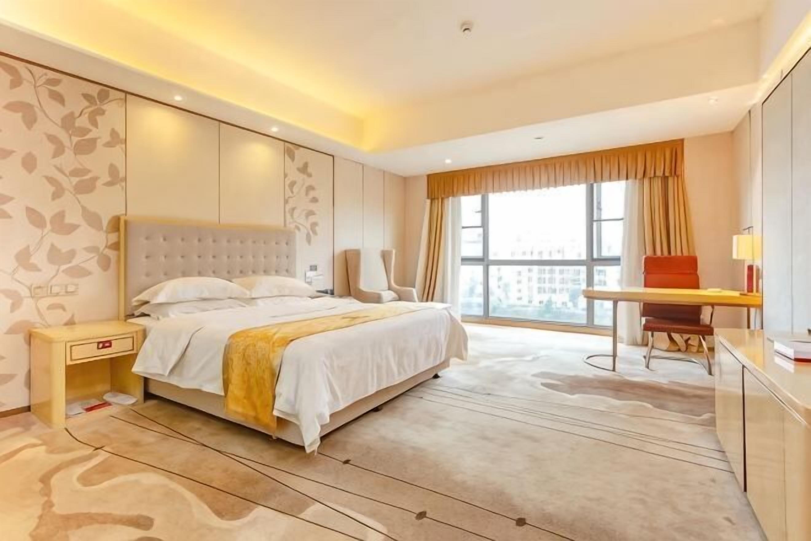 A hotel room with a large bed, a desk, a chair, and a view of the city.