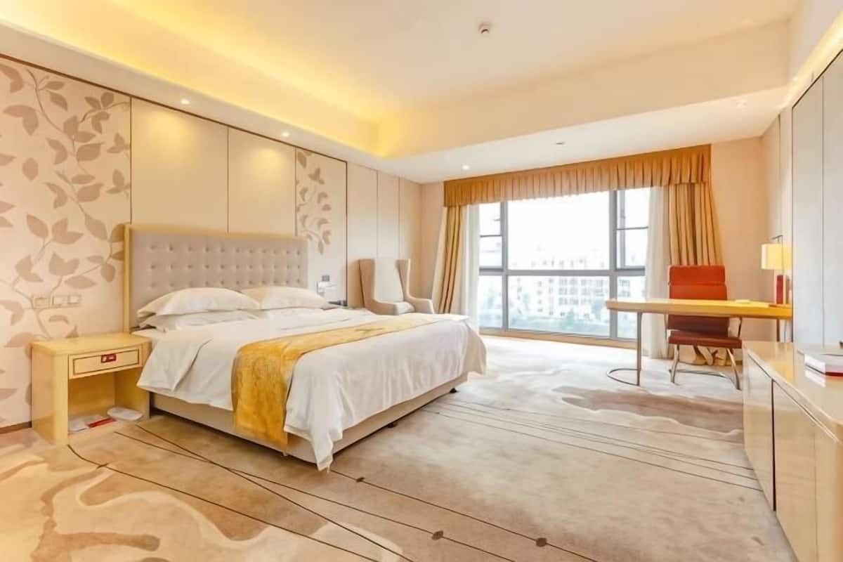 A hotel room with a large bed, a desk, a chair, and a view of the city.