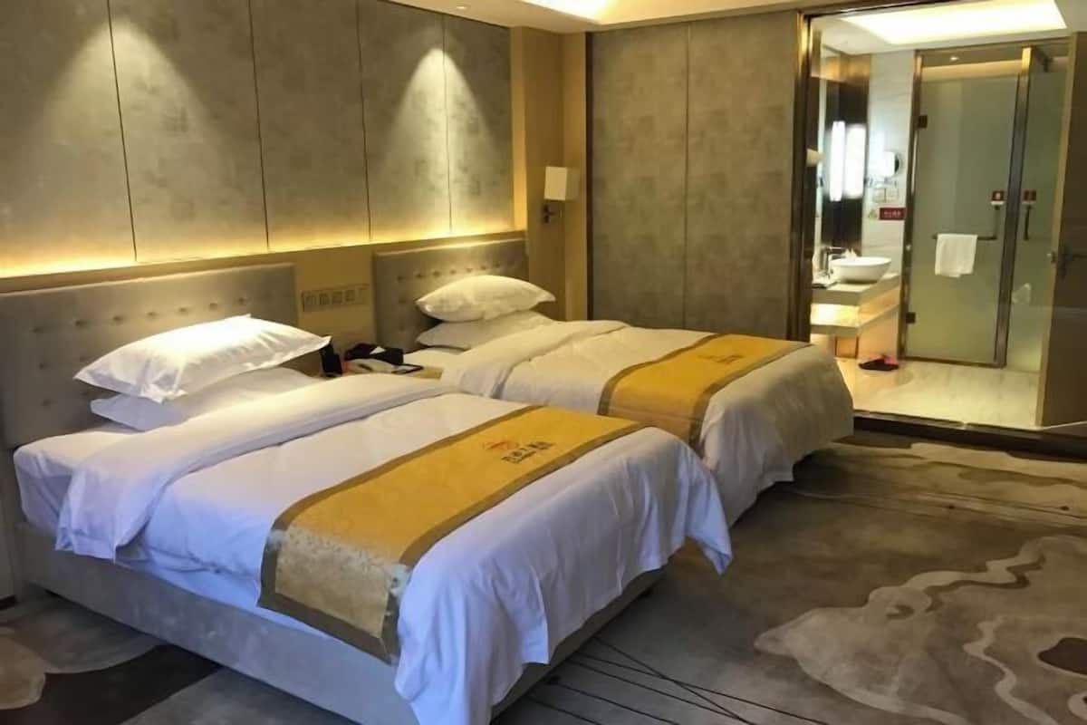 A hotel room with two beds, a large mirror, a bathroom with a sink and shower, and a carpeted floor.