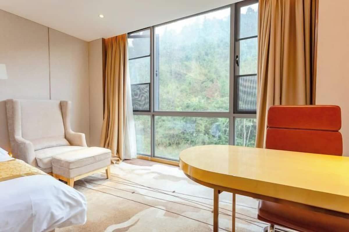 A hotel room with a large window, a bed, a chair, and a table.
