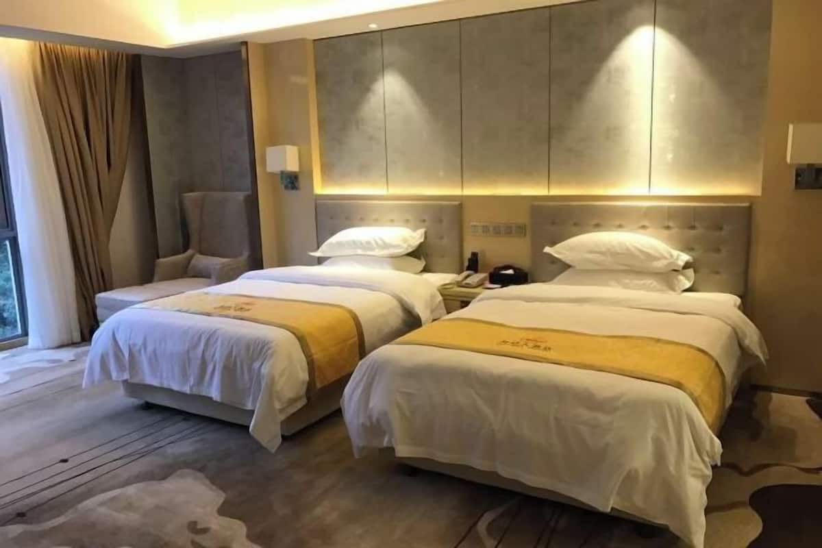 A hotel room with two beds, a chair, a nightstand, and a large window.