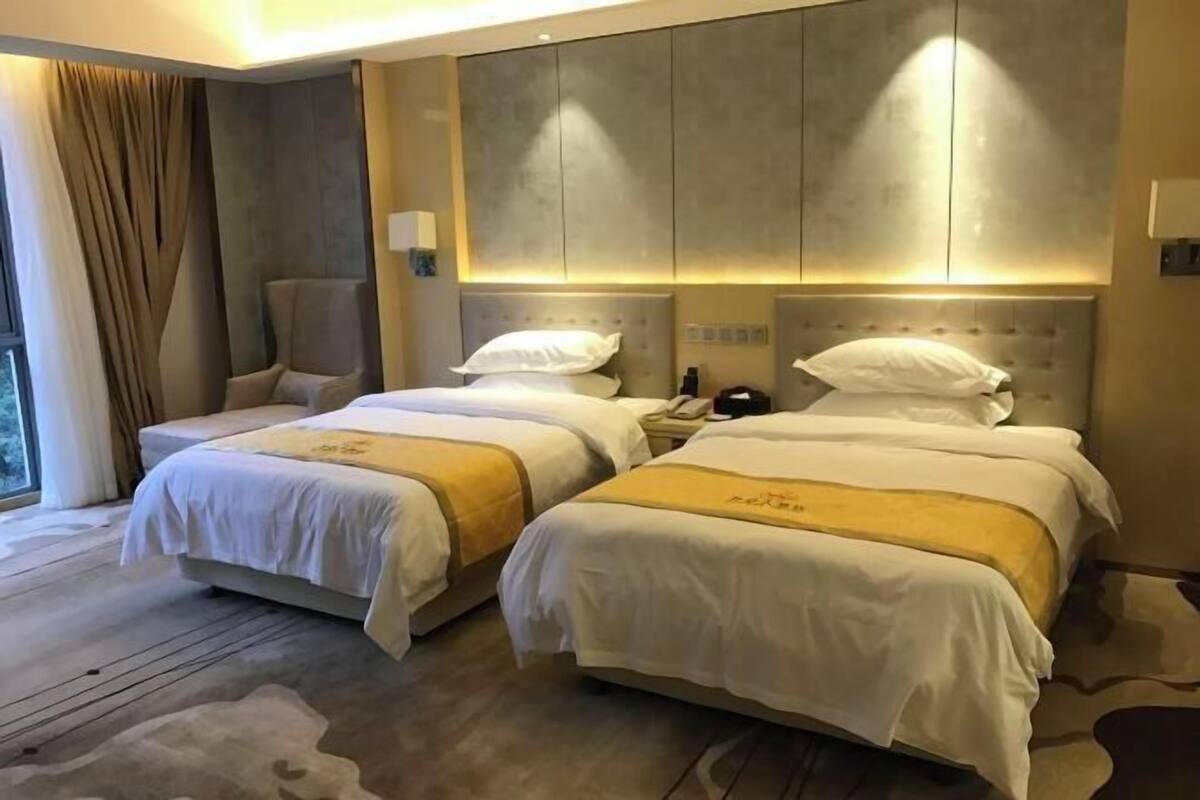 A hotel room with two beds, a large window, and a chair.