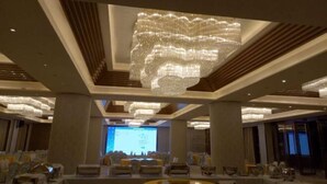 Un salón de conferencias con una lámpara araña grande y moderna, filas de sillas y una pantalla de presentación.