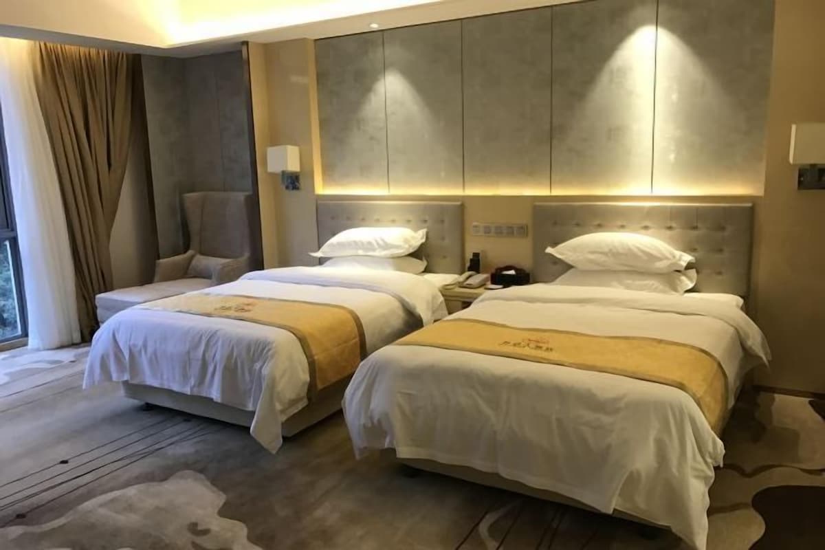 A hotel room with two beds, a large window, and a chair.