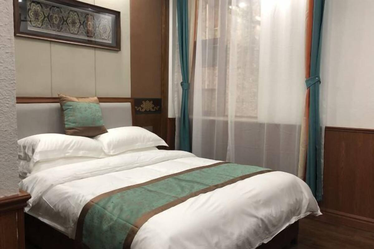 Ein ordentlich gemachtes Bett mit weißer und grüner Bettwäsche, einem Holz-Kopfteil und einem dekorativen Wandbild darüber.