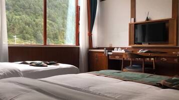 Habitación de hotel con dos camas, un escritorio con silla, televisión y ventana con vista al bosque.